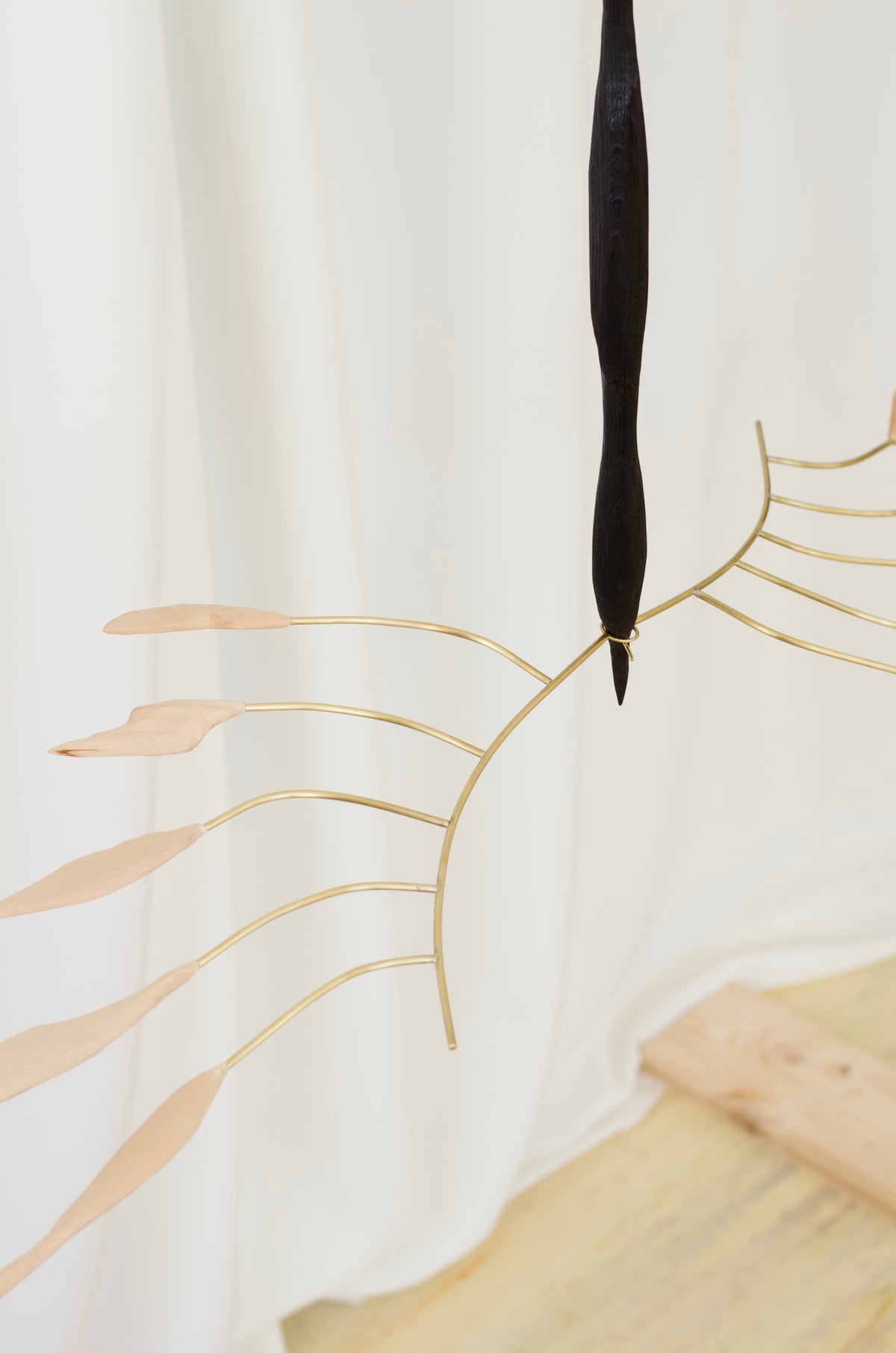 artistic hanging object with a tanned wood base and brass rods that look like wings on a white background